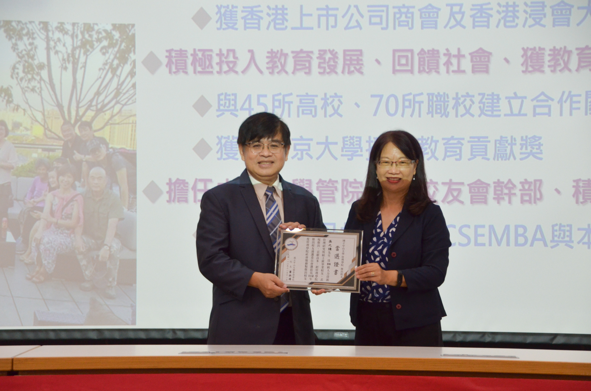 112年度管院傑出校友吳之煒學長，因不克前來，由EMBA執行長林豪傑（左）代為領獎，管院葉淑娟院長頒贈獎狀與獎盃圖片