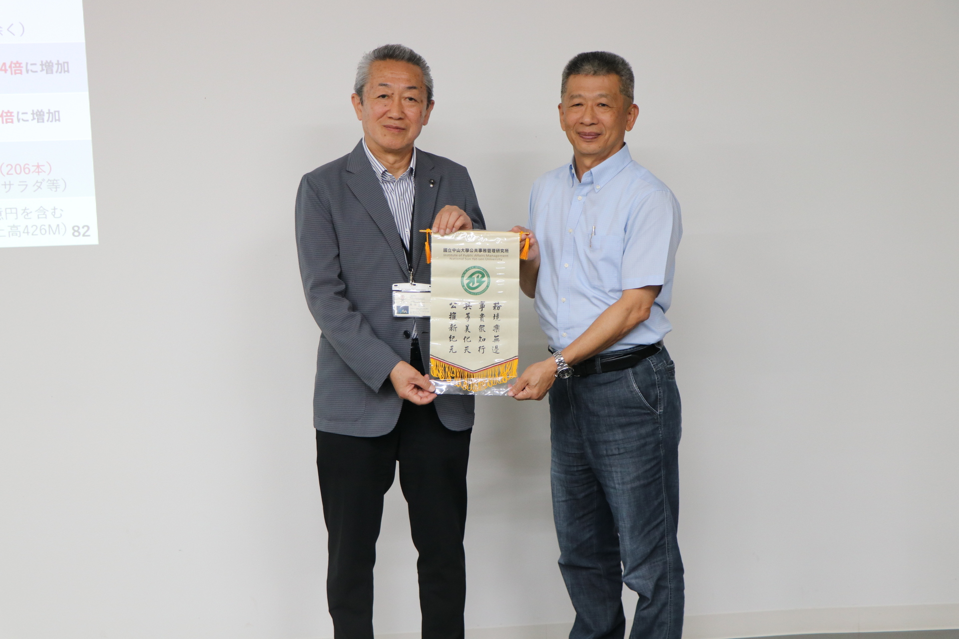 中山大學公事所郭瑞坤教授(圖右)致贈錦旗予大洲市地域振興聯盟理事長髙岡公三(圖左)，並與理事長相互交流有關於城下町活化和歷史建築再利用之經驗。圖片